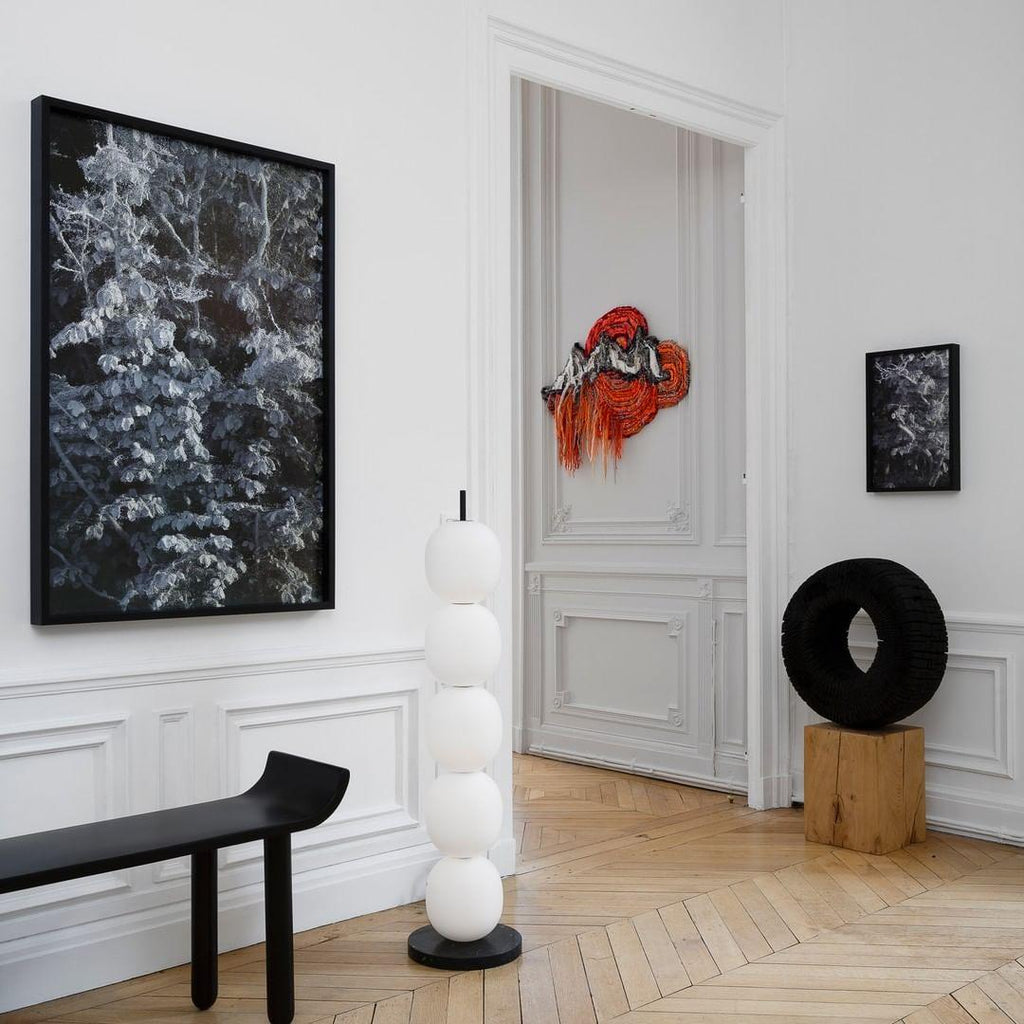 Unlit lamp in a panelled hall between a black bench and an open doorway, on parquet.
