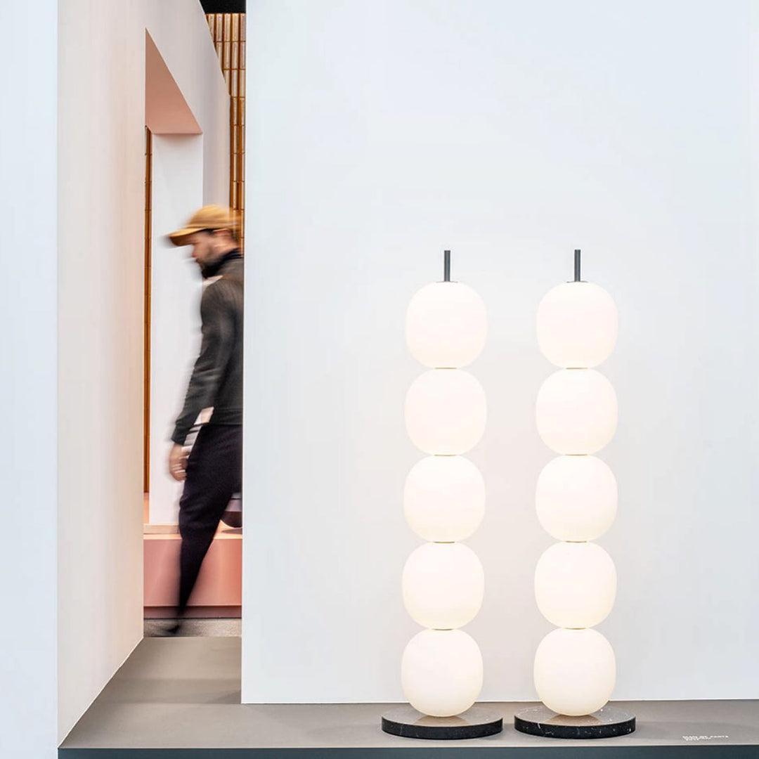 Two unlit lamps side by side on a grey display ledge, a visitor passing in blur behind them.