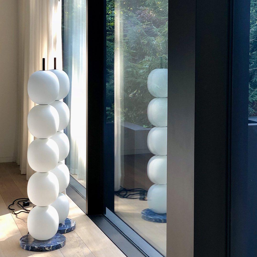 Two unlit lamps by a glass door, their stacks mirrored in the pane with the garden beyond.
