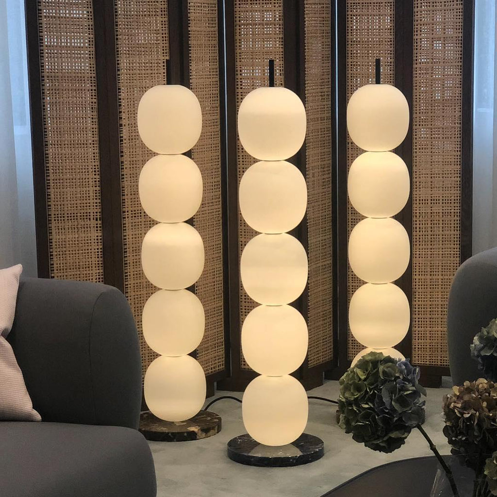 Three lamps lit in a row against a woven cane screen, with a grey sofa and hydrangeas alongside.