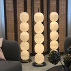 Three lamps lit in a row against a woven cane screen, with a grey sofa and hydrangeas alongside.