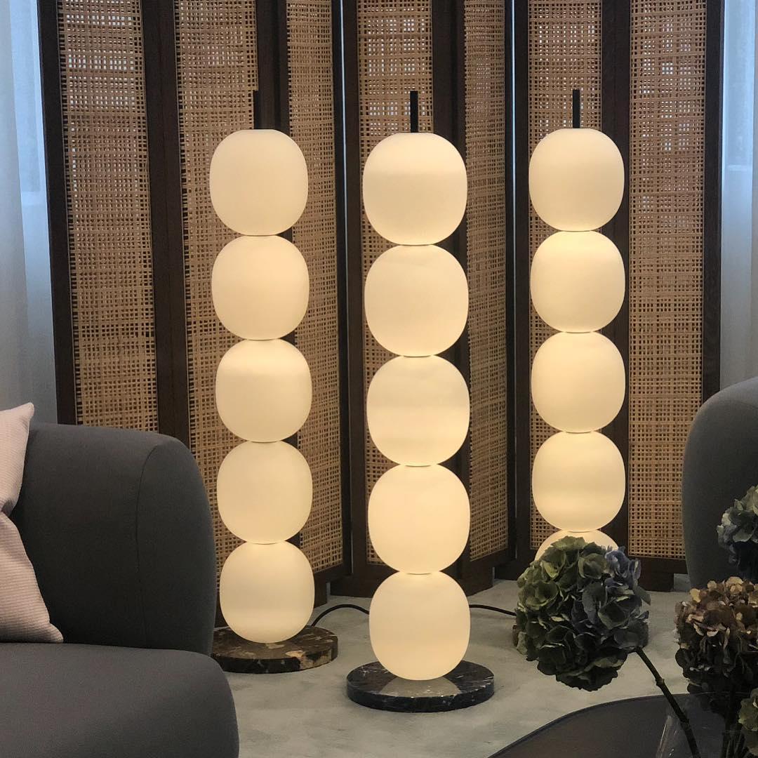 Three lamps lit in a row against a woven cane screen, with a grey sofa and hydrangeas alongside.