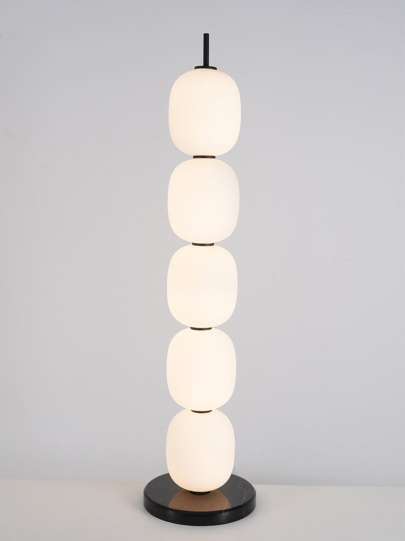 The unlit lamp on a white surface against pale grey, black stem upright above the top globe.