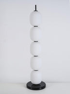 Unlit lamp on a white plinth against a marked grey studio wall, seen slightly from the side.