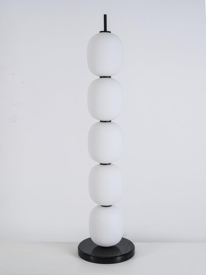 Unlit lamp on a white plinth against a marked grey studio wall, seen slightly from the side.