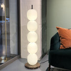 Lit lamp on a red veined marble base against white brick, next to a green velvet chair.