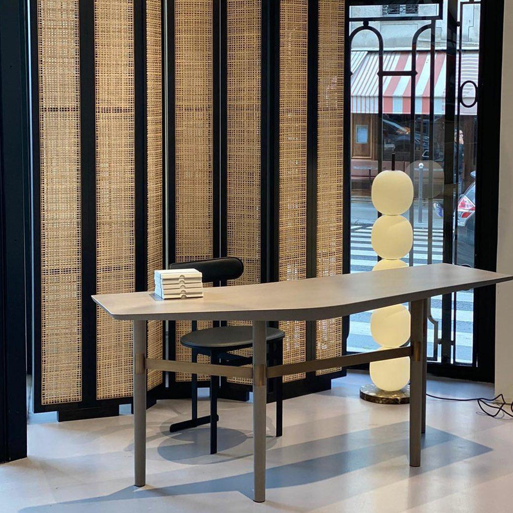 Lit lamp seen behind a long console table in a showroom, its middle globe hidden by the tabletop.