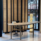 Lit lamp seen behind a long console table in a showroom, its middle globe hidden by the tabletop.