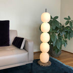 Lit lamp on a brown marble base between a beige leather sofa and a potted plant, on a blue rug.