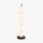Studio view of the unlit floor lamp, five opal glass globes stacked on a black marble disc base.