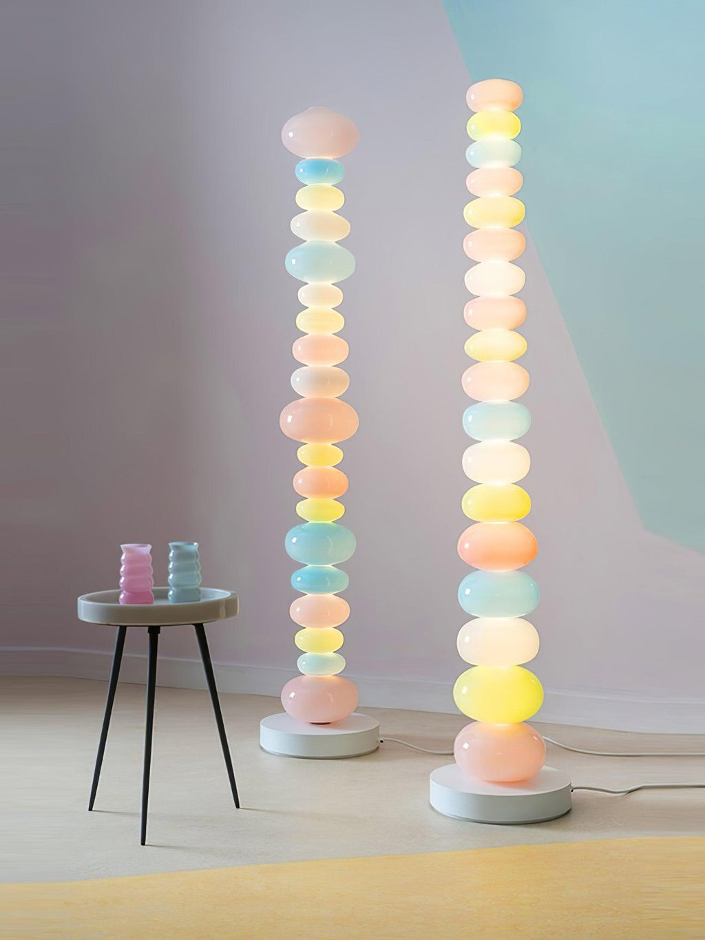 Two Clérachic floor lamps stand side by side near a round table set with glassware against a lilac-grey wall.