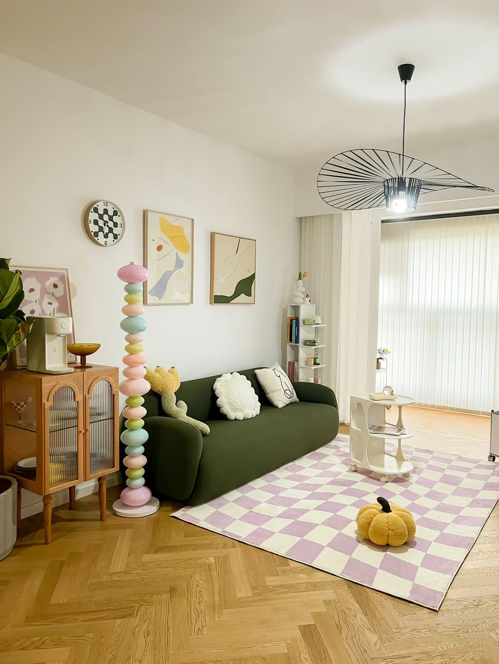 Beside a deep green sofa and a checked lilac rug, this Clérachic floor lamp's globe column glows near open bookshelves.