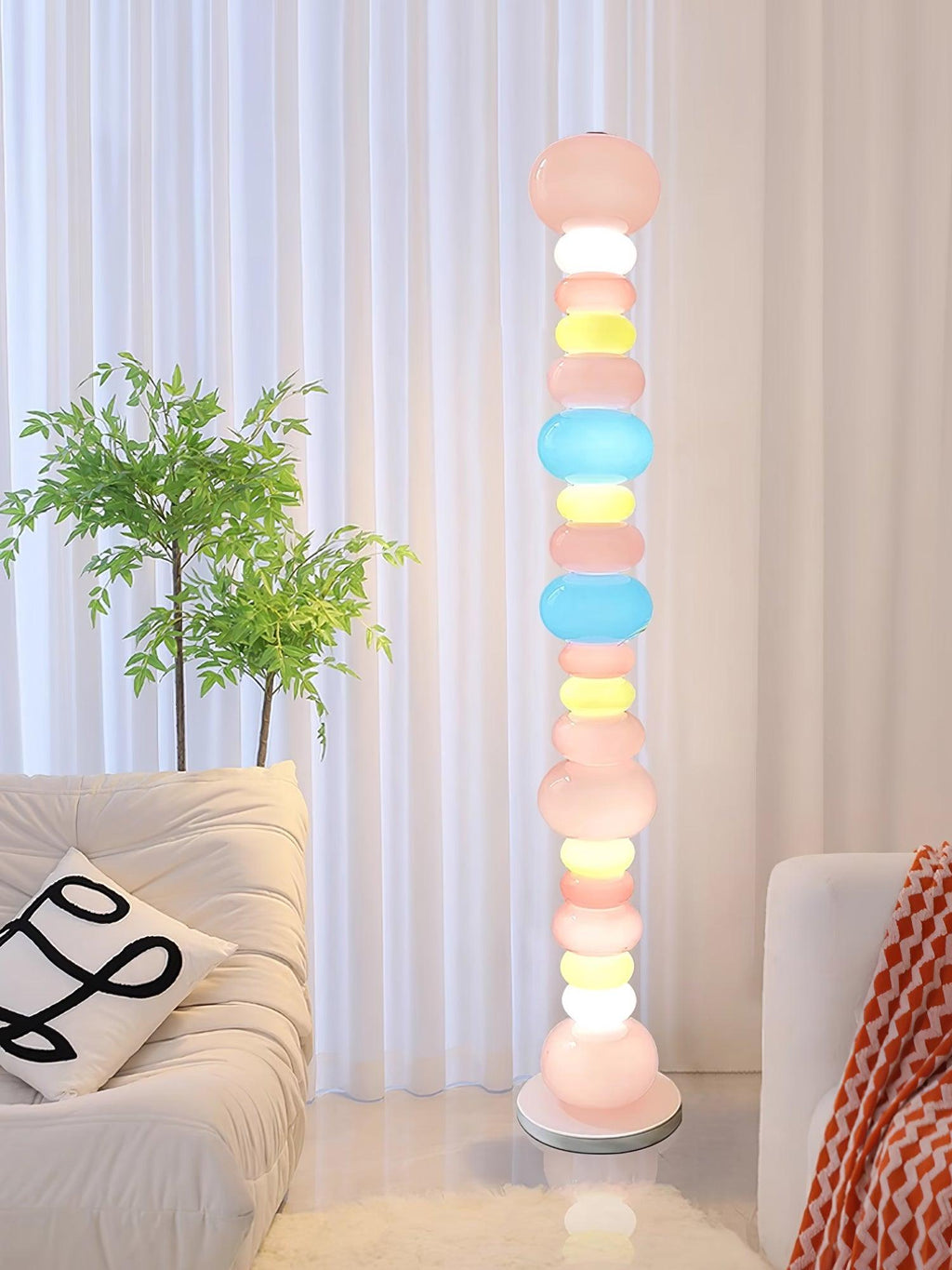 Beside a cream sofa with a patterned cushion and a potted plant, this Clérachic floor lamp glows near sheer curtains.