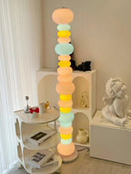Beside a round side table and a small statue, this Clérachic floor lamp's globe column glows near open white shelving.