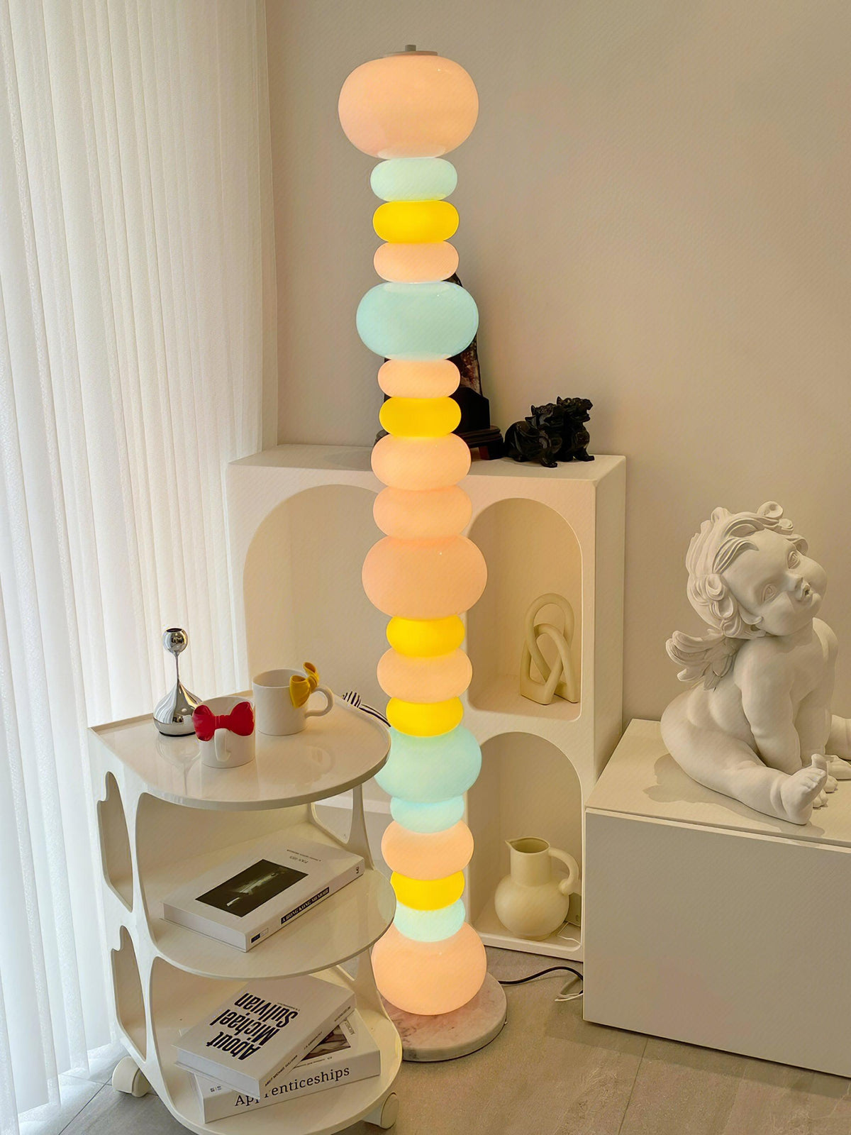 Beside a round side table and a small statue, this Clérachic floor lamp's globe column glows near open white shelving.