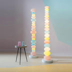 Two Clérachic floor lamps stand together near a round side table set with blue glassware against a soft lilac wall.