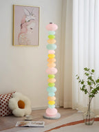 Under a pink portrait print and near a floral cushion, this Clérachic floor lamp's globe column glows beside a plant.