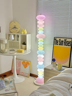 Under a wall clock and sun-print poster, this Clérachic floor lamp's crown globe glows pink above the stacked column.