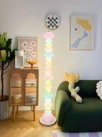 Beside a green sofa and a rattan cabinet, this Clérachic floor lamp's globe column glows under a round wall clock.
