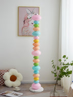 Under a framed portrait print and beside a floral cushion, this Clérachic floor lamp's globe column glows near a plant.