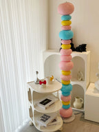 Clérachic multicolour floor lamp lit beside a white shelving unit stacked with books and mugs.