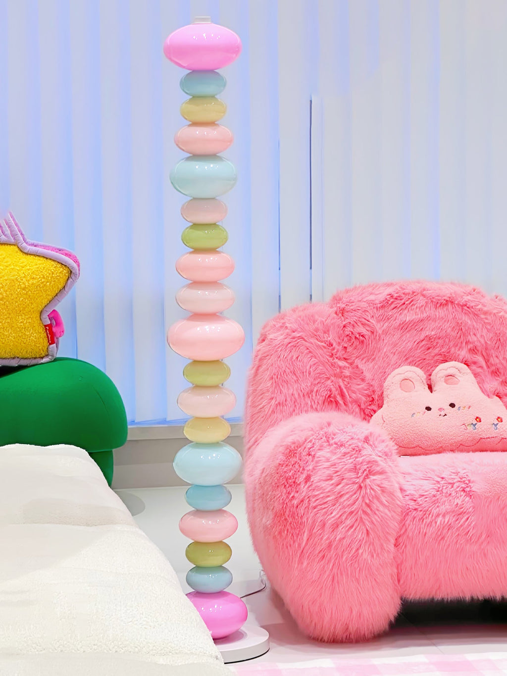 Clérachic multicolour floor lamp lit beside a pink fluffy armchair holding a bunny plush toy, in a pastel child's room.