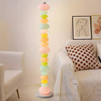 Clérachic multicolour floor lamp lit beside a cream armchair with a polka-dot cushion and framed portrait prints.