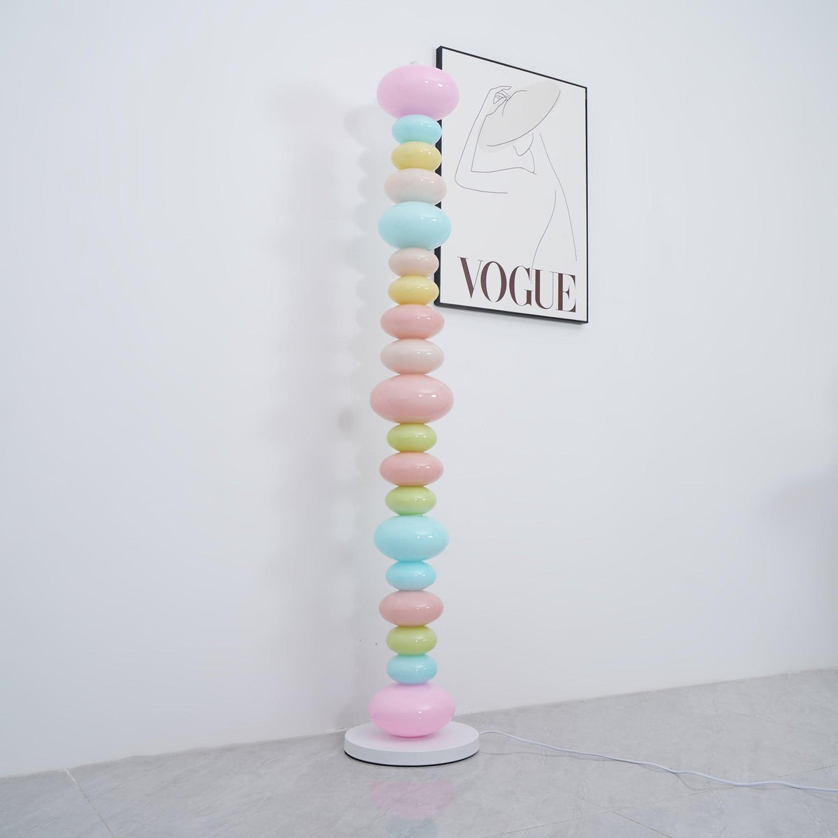 Clérachic glass globe floor lamp shown unlit in daylight beside a 'VOGUE' wall print, its pastel colours flat and matte.