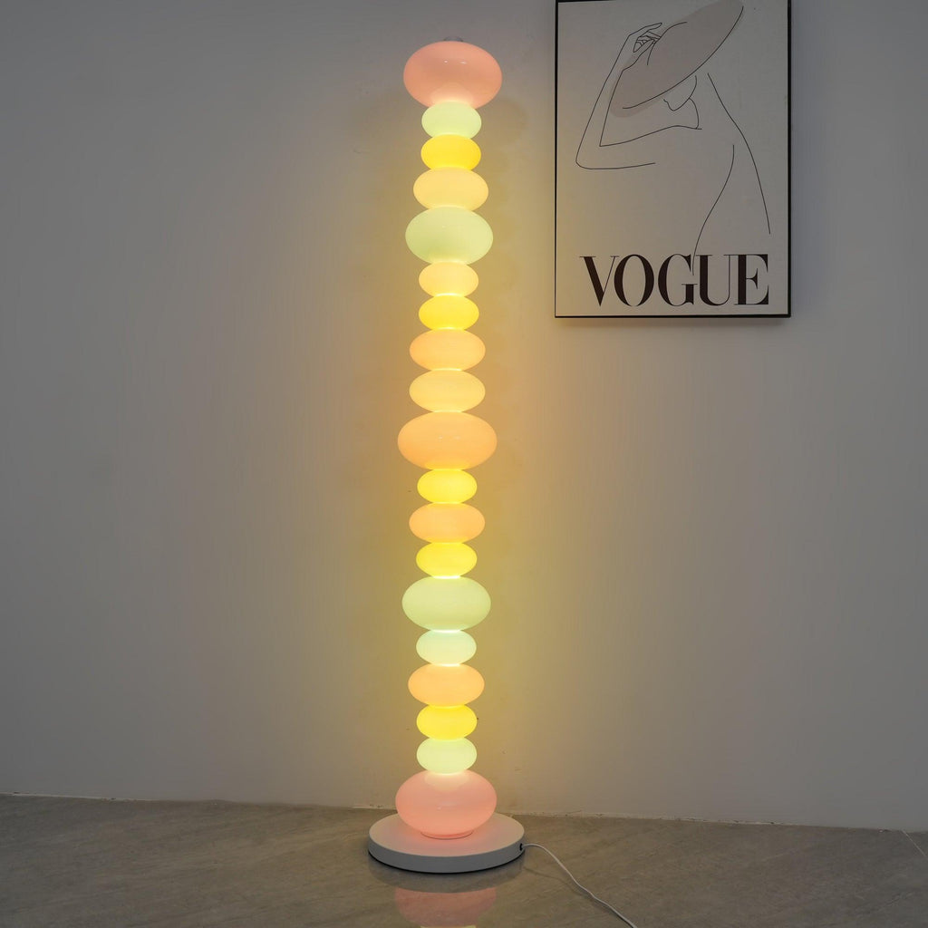Clérachic multicolour floor lamp lit against a plain wall beneath a framed 'VOGUE' print, on a bare concrete floor.