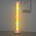 Clérachic multicolour floor lamp lit against a plain wall beneath a framed 'VOGUE' print, on a bare concrete floor.