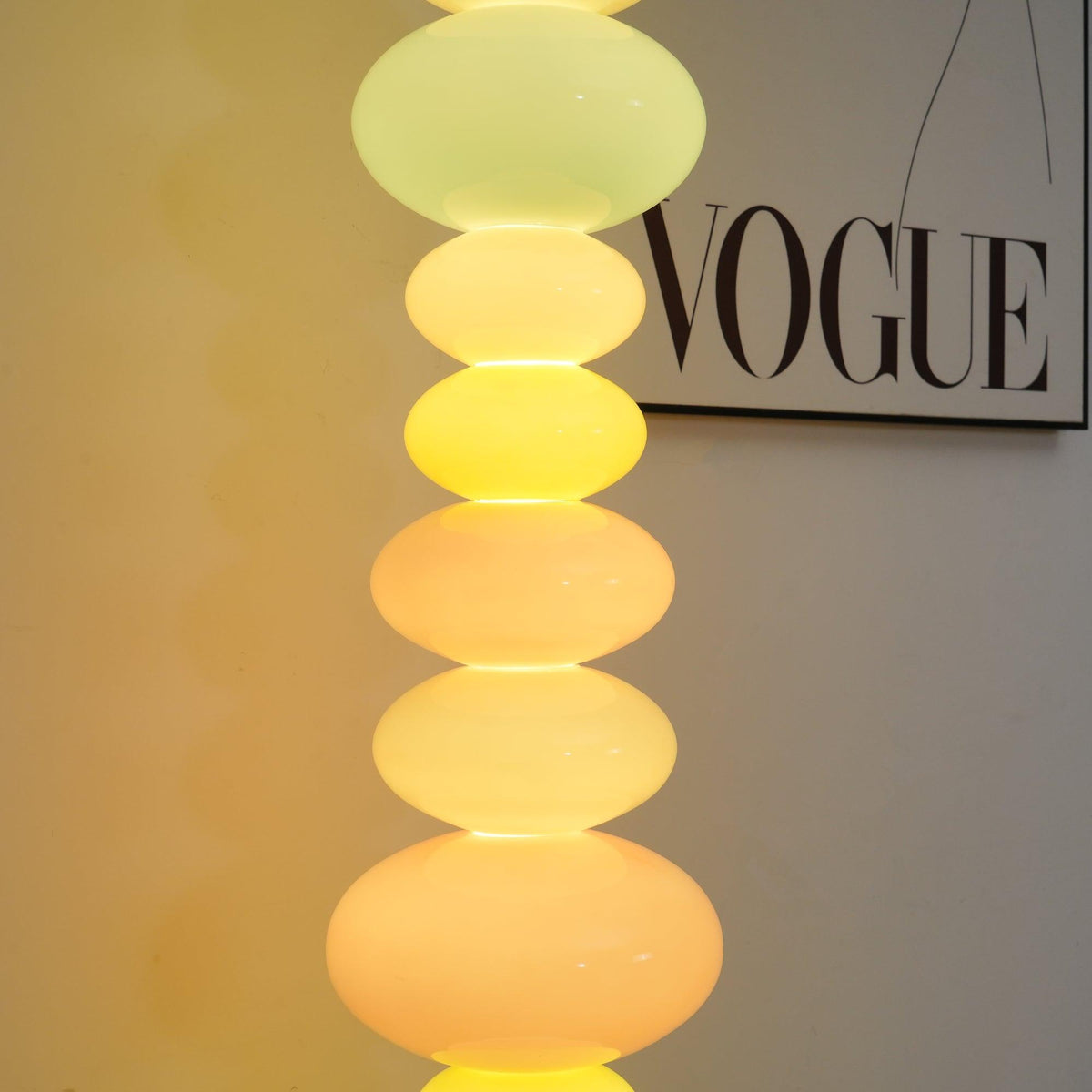 Close crop of a Clérachic glass globe lamp's top orbs glowing warm yellow, with a 'VOGUE' print visible behind.