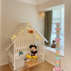 Clérachic pastel floor lamp lit beside a children's playhouse bed frame strung with fairy lights and soft toys.
