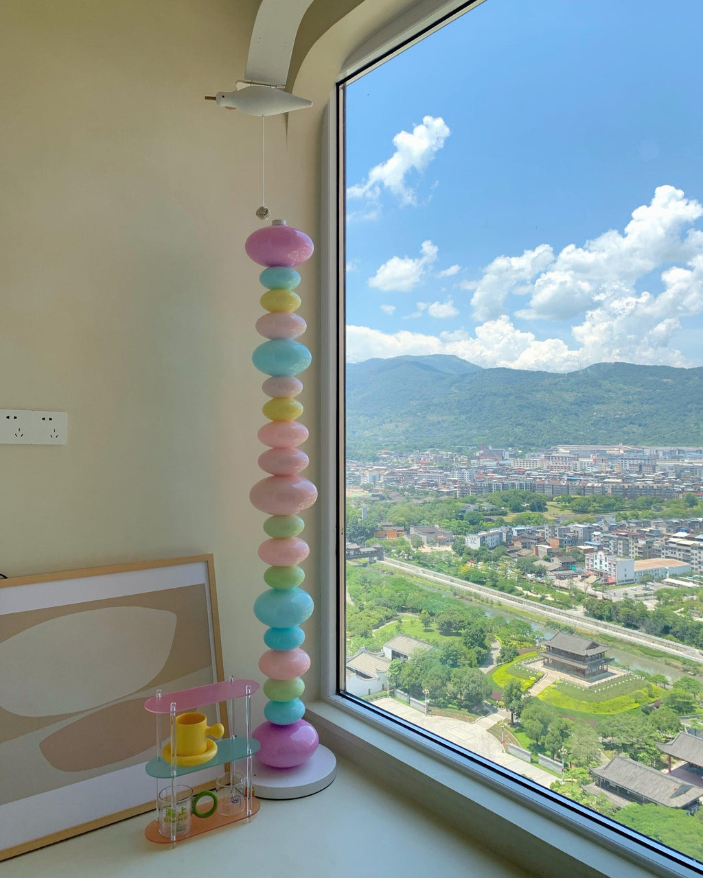 Clérachic glass globe floor lamp lit beside a floor-to-ceiling window overlooking distant hills and rooftops.