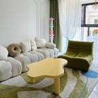 Clérachic pastel floor lamp glowing beside a cream sofa and a green boucle chair on a wavy-patterned rug.