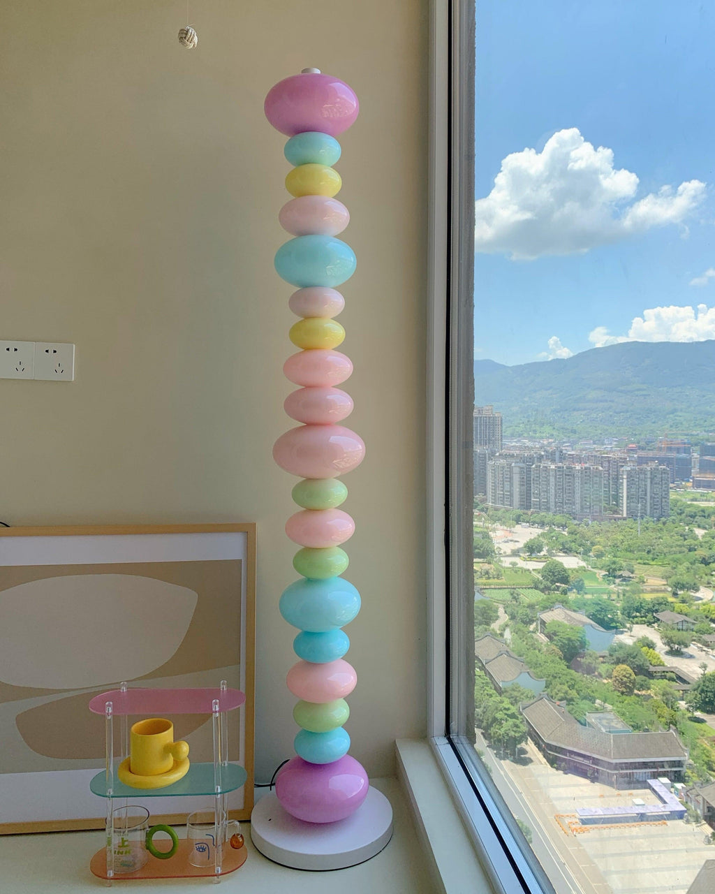 Clérachic stacked glass globe lamp lit beside a floor-to-ceiling window with a distant hillside and skyline view.