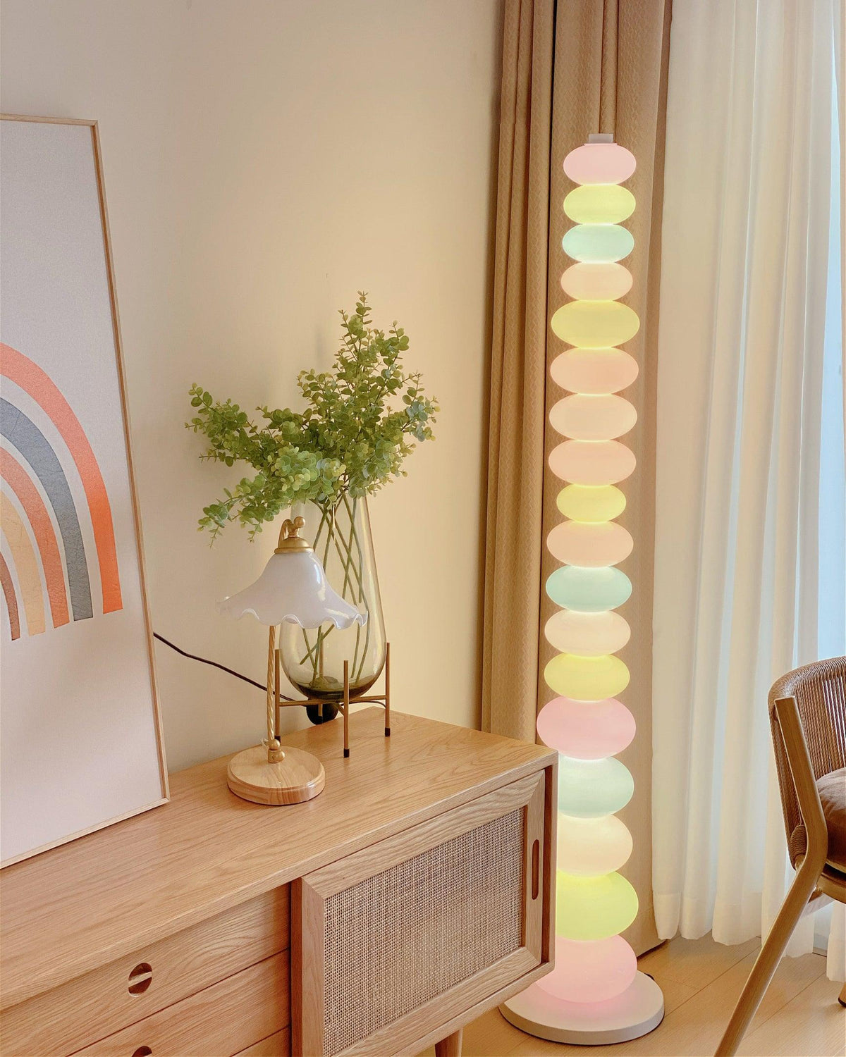 Clérachic multicolour floor lamp lit beside a wooden dresser, a rainbow print on the wall and a rattan chair.