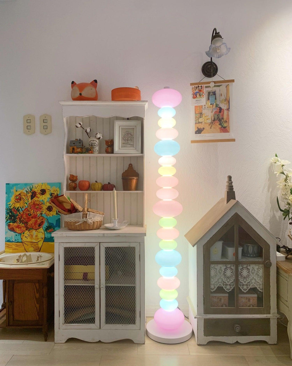 Clérachic pastel floor lamp glowing beside a bookshelf and dollhouse, with a sunflower painting on the wall.