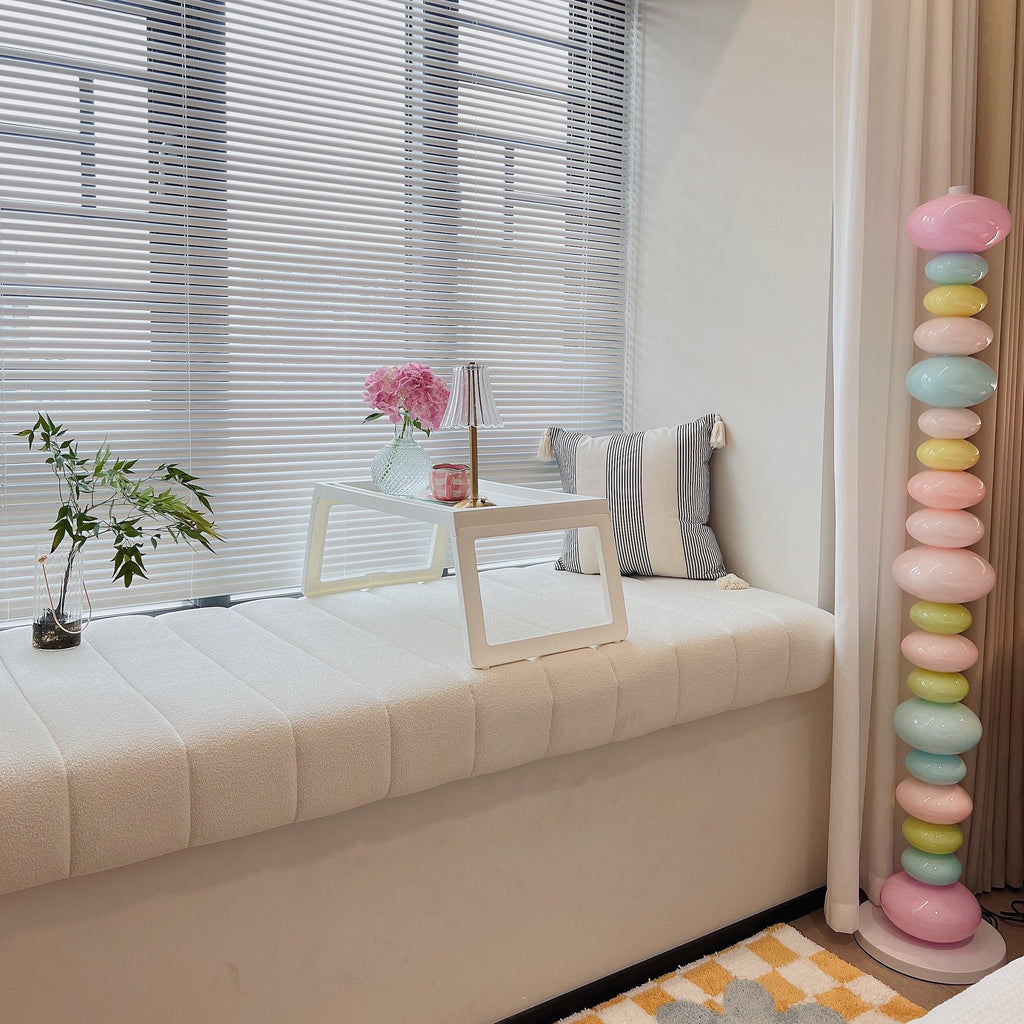 Clérachic multicolour floor lamp lit in a window seat nook with patterned cushions and closed venetian blinds.