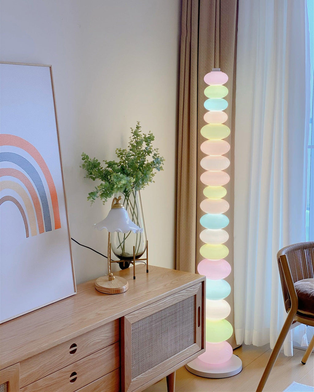 Clérachic stacked glass globe floor lamp lit beside a wooden cabinet, a small table lamp and a rainbow print.