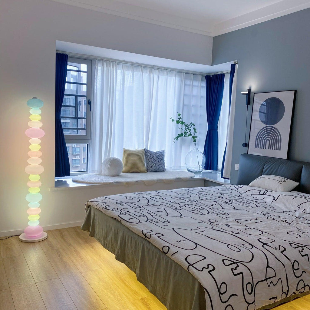 Clérachic multicolour floor lamp lit in a bay-window bedroom with doodle-print bedding and navy curtains.