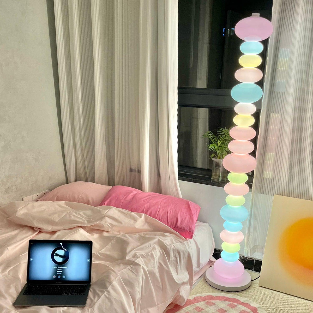 Clérachic glass globe floor lamp glowing in a bedroom with pink bedding, framed wall art and an open laptop.