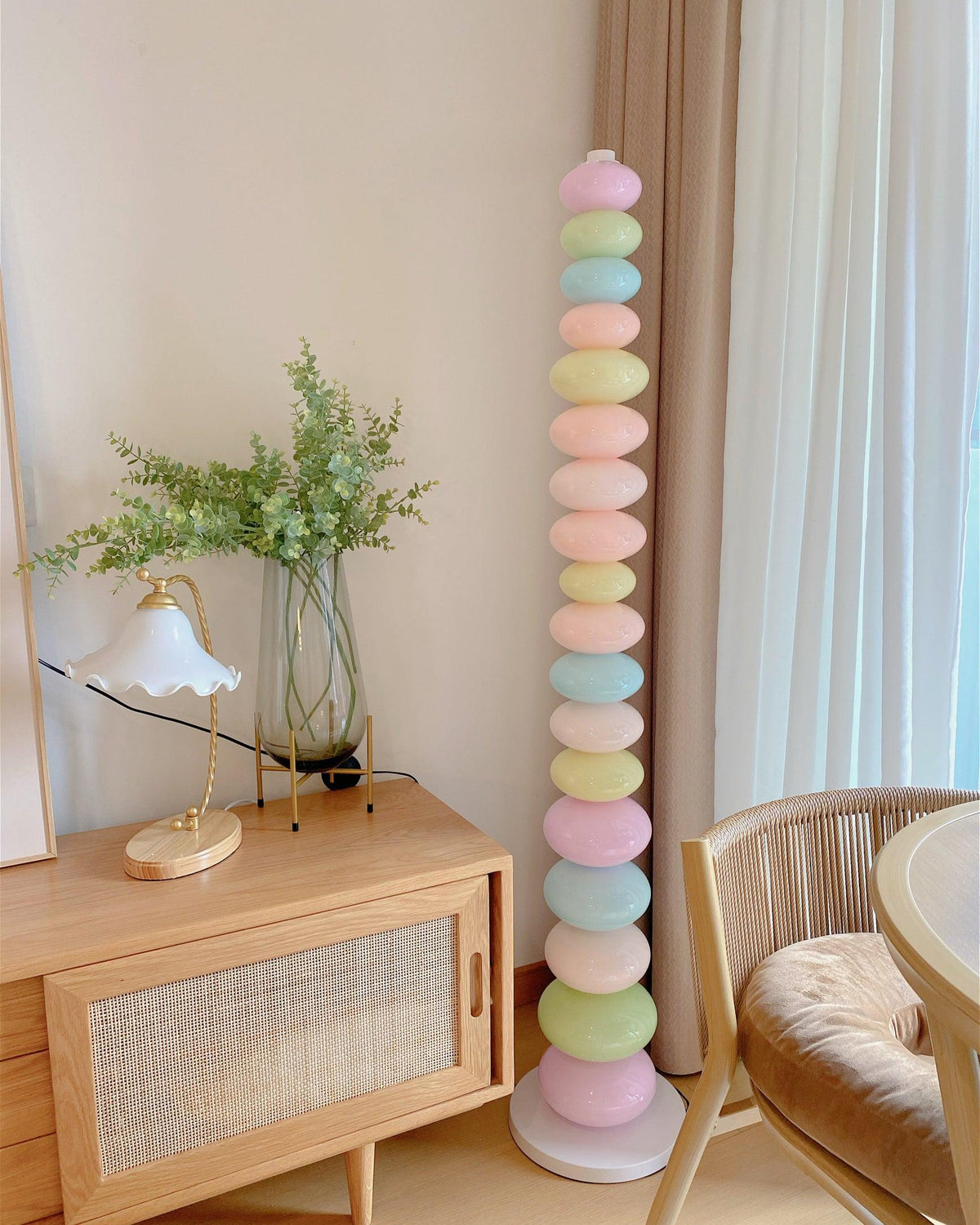 Clérachic pastel floor lamp glowing beside a wooden console table, a small lamp and rattan dining chairs.