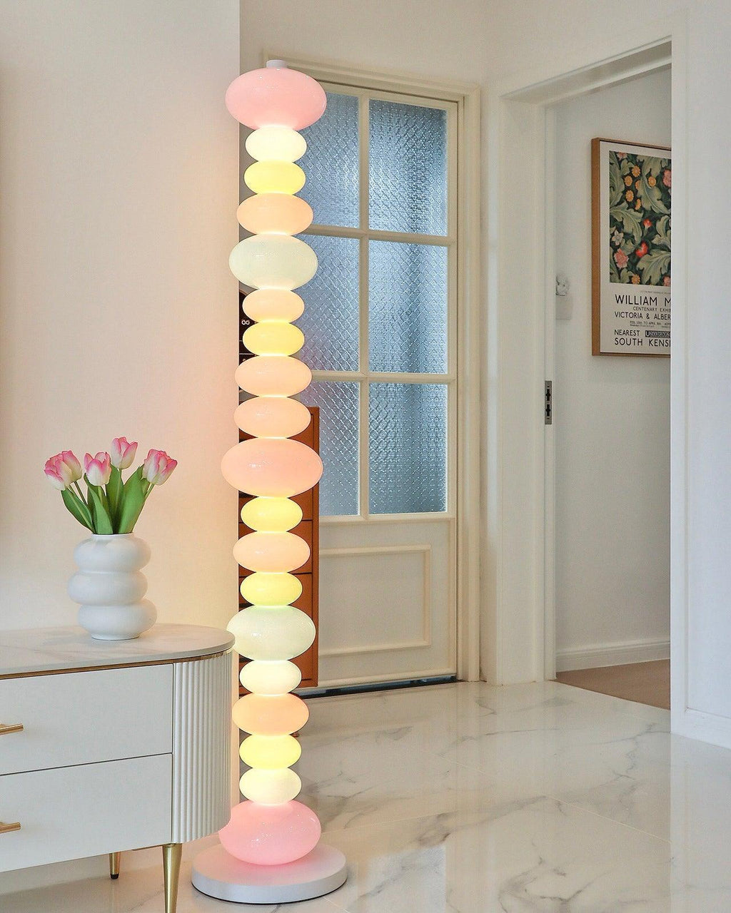Clérachic multicolour floor lamp lit beside a white dresser with a tulip vase, near a glazed panelled door.
