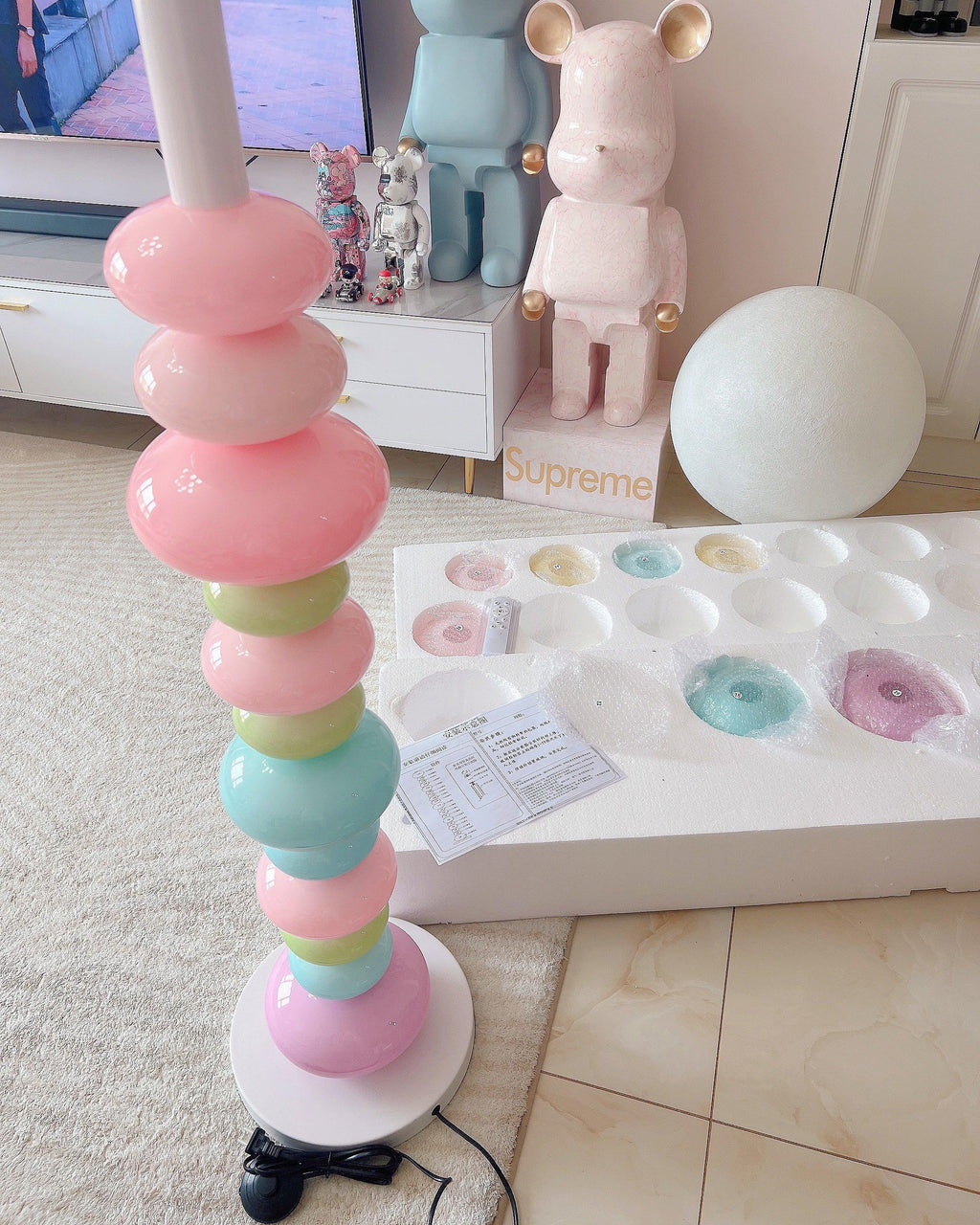 Close crop of a Clérachic glass globe lamp's lower orbs beside its open foam packaging insert and a collectible figure.