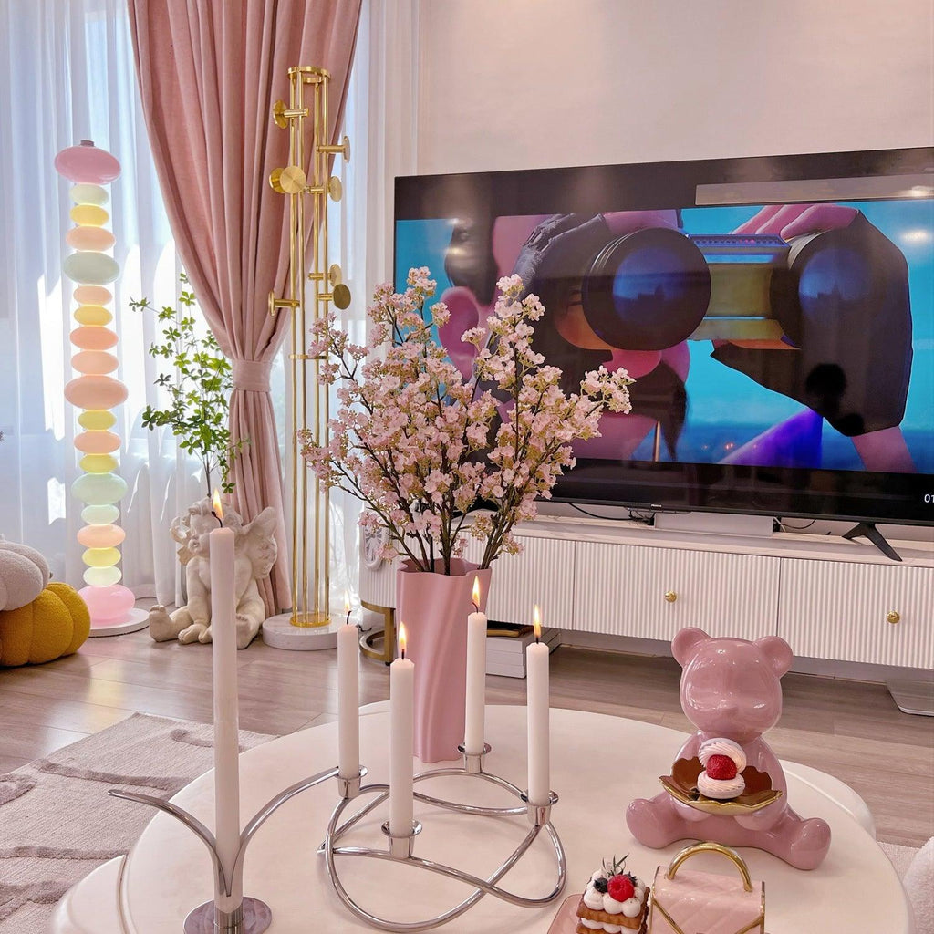 Clérachic stacked glass globe lamp lit beside a TV stand styled with pink candles, a cake stand and a teddy bear.