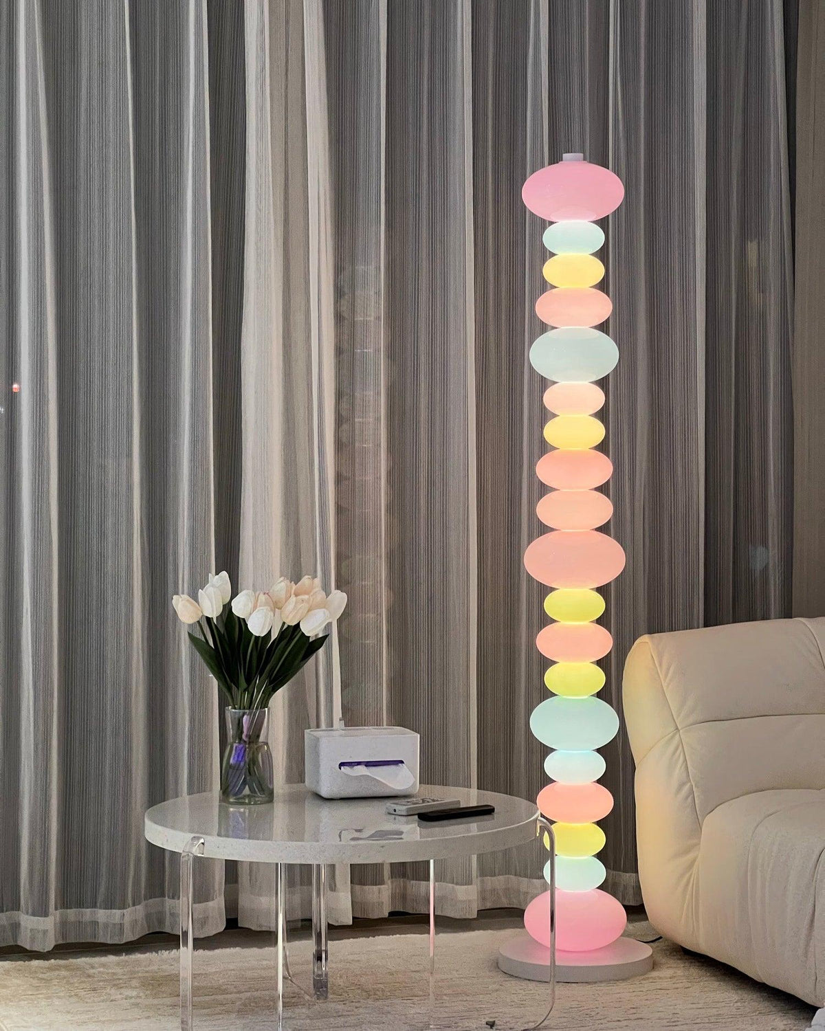 Clérachic pastel floor lamp glowing beside a glass-topped coffee table and sheer curtains in a bright living room.