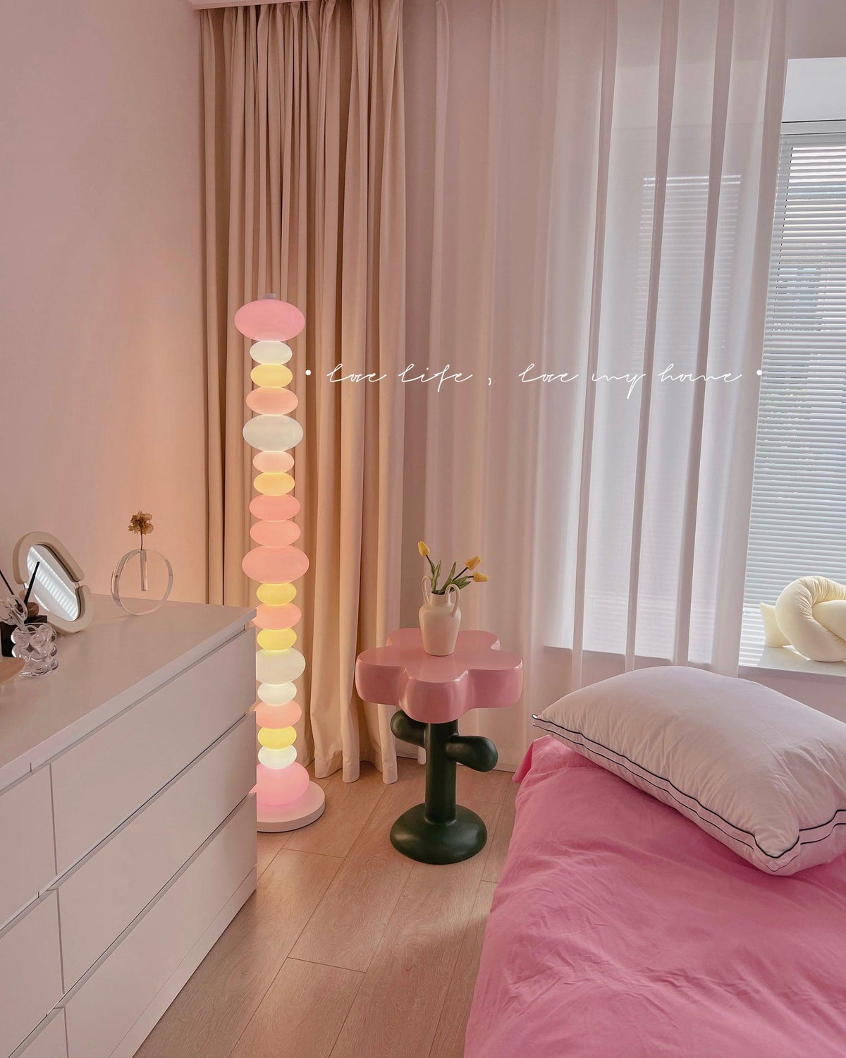 Clérachic glass globe floor lamp glowing in a pink-toned bedroom, beside a round mirror and a flower-shaped stool.