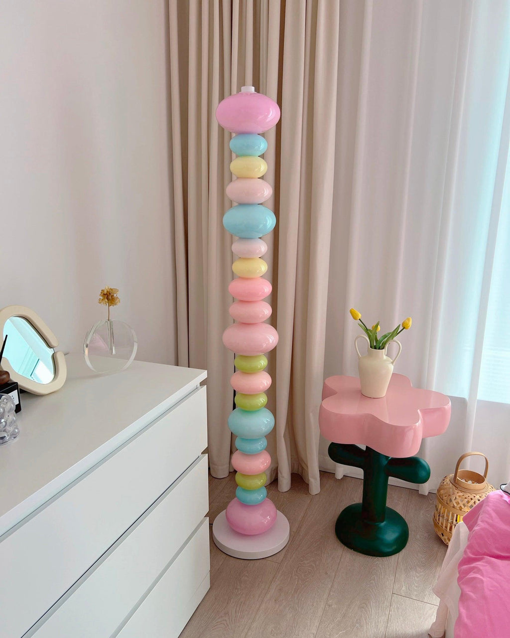 Clérachic pastel floor lamp glowing beside a white dresser, a round mirror and pink bedding just visible behind.