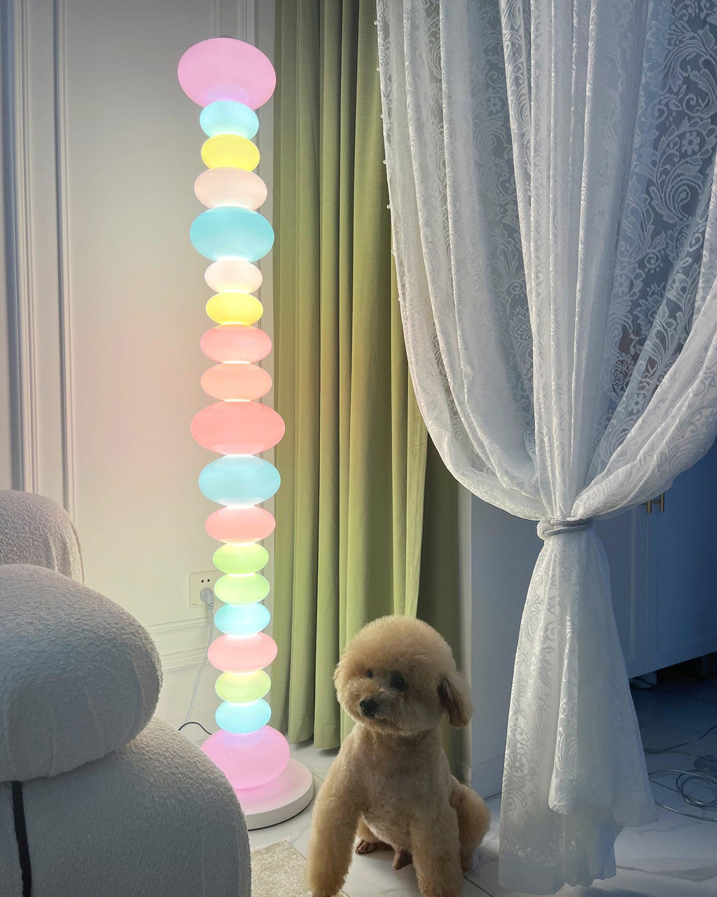 A small dog sits near this Clérachic floor lamp, its lit glass globes rising beside sheer green curtains in a living room.