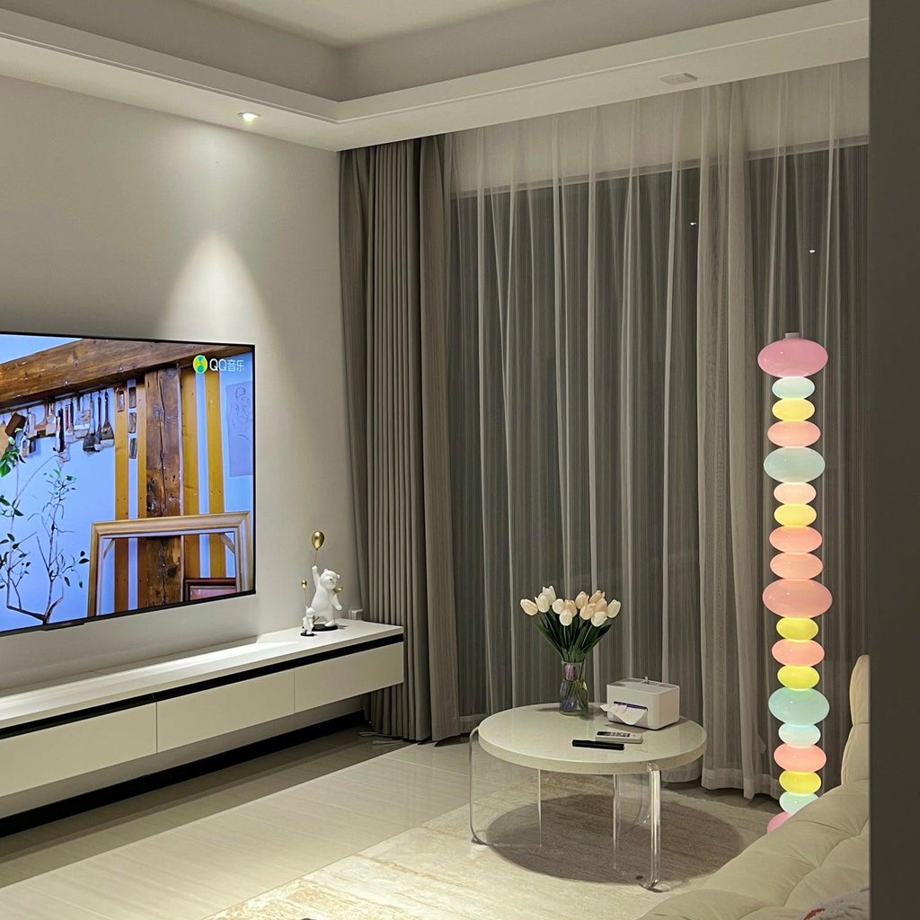 A vase of tulips sits on a round coffee table as this Clérachic floor lamp glows beside a wall-mounted television.